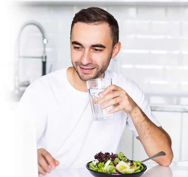 Man eating a salad and drinking water in his kitchen