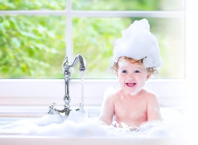 Small child taking a soapy bubble bath with running water